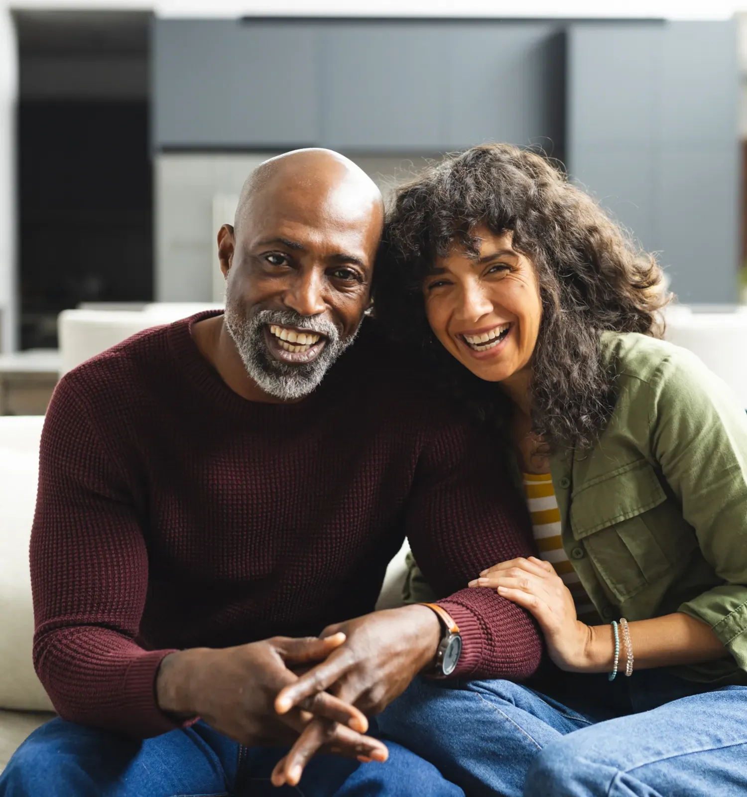 The Ensley 55+ Luxury Apartments with Smiling man and woman sitting closely together on a couch in a modern living room.