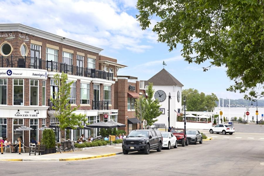 The Ensley 55+ Luxury Apartments with Street view of a lakeside town with shops, parked cars, outdoor dining, and a white clock tower.