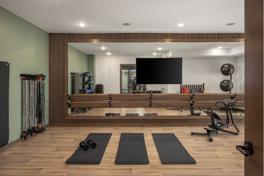 The Ensley 55+ Luxury Apartments with Modern gym room with three yoga mats, dumbbells, resistance bands, a stationary bike, and a large wall mirror.