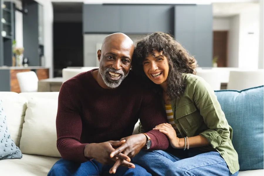 The Ensley 55+ Luxury Apartments with Smiling man and woman sitting closely together on a couch in a modern living room.