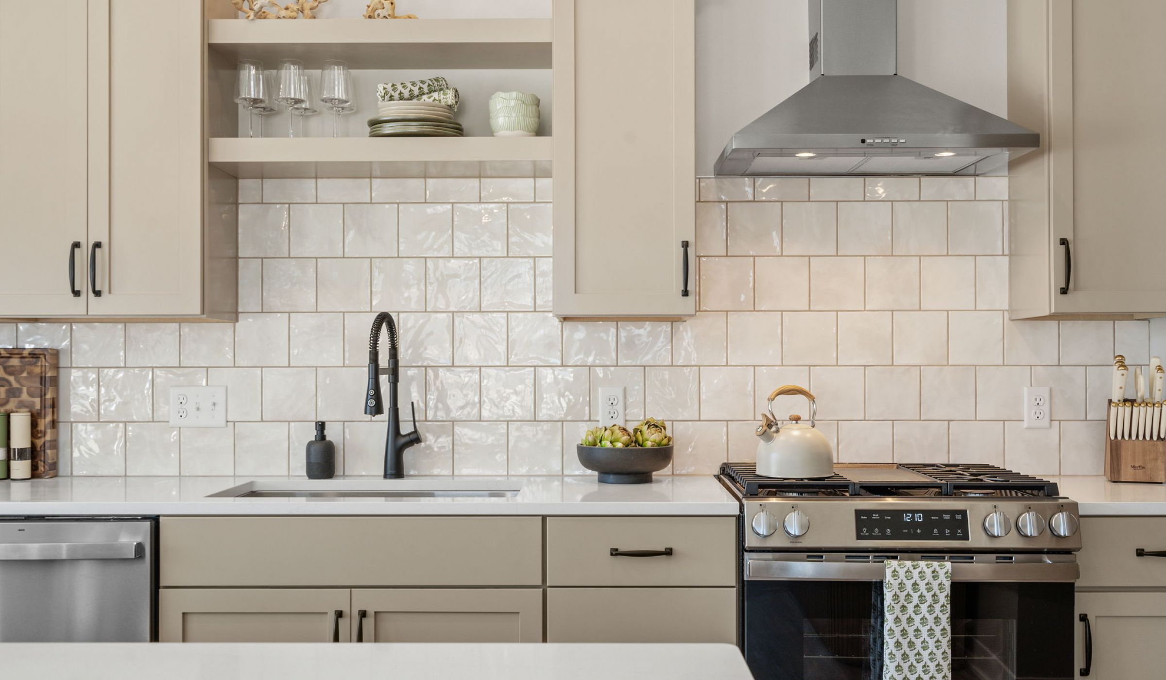 The Ensley 55+ Luxury Apartments with Modern kitchen with beige cabinets, tiled backsplash, stove, sink, and open shelves with dishes and decor.