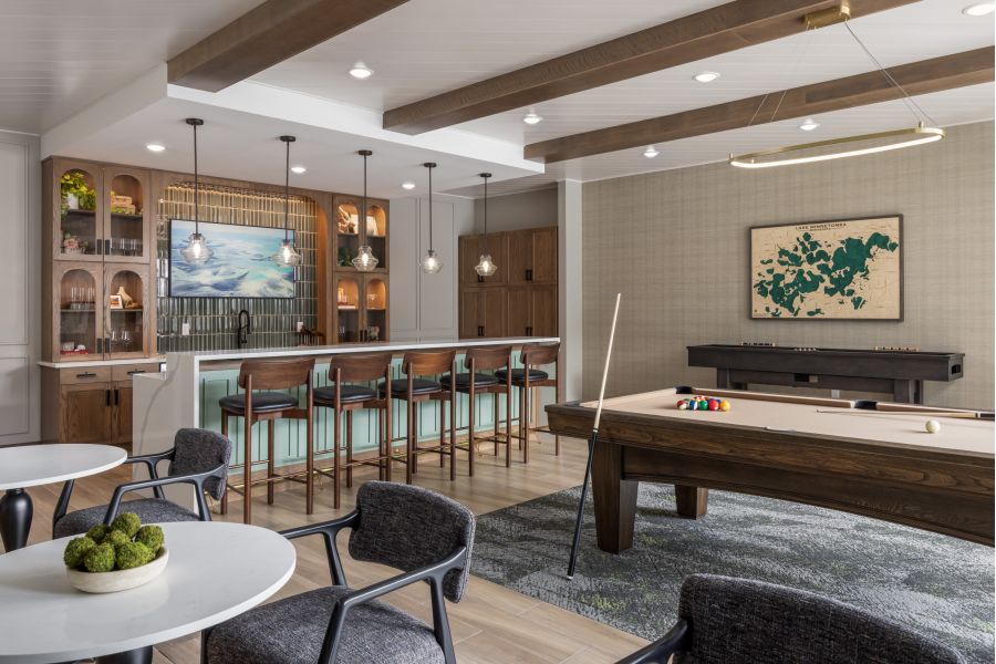 The Ensley 55+ Luxury Apartments with Modern game room with pool table, shuffleboard, bar seating, wall art, and stylish lighting, featuring wood and neutral tones.