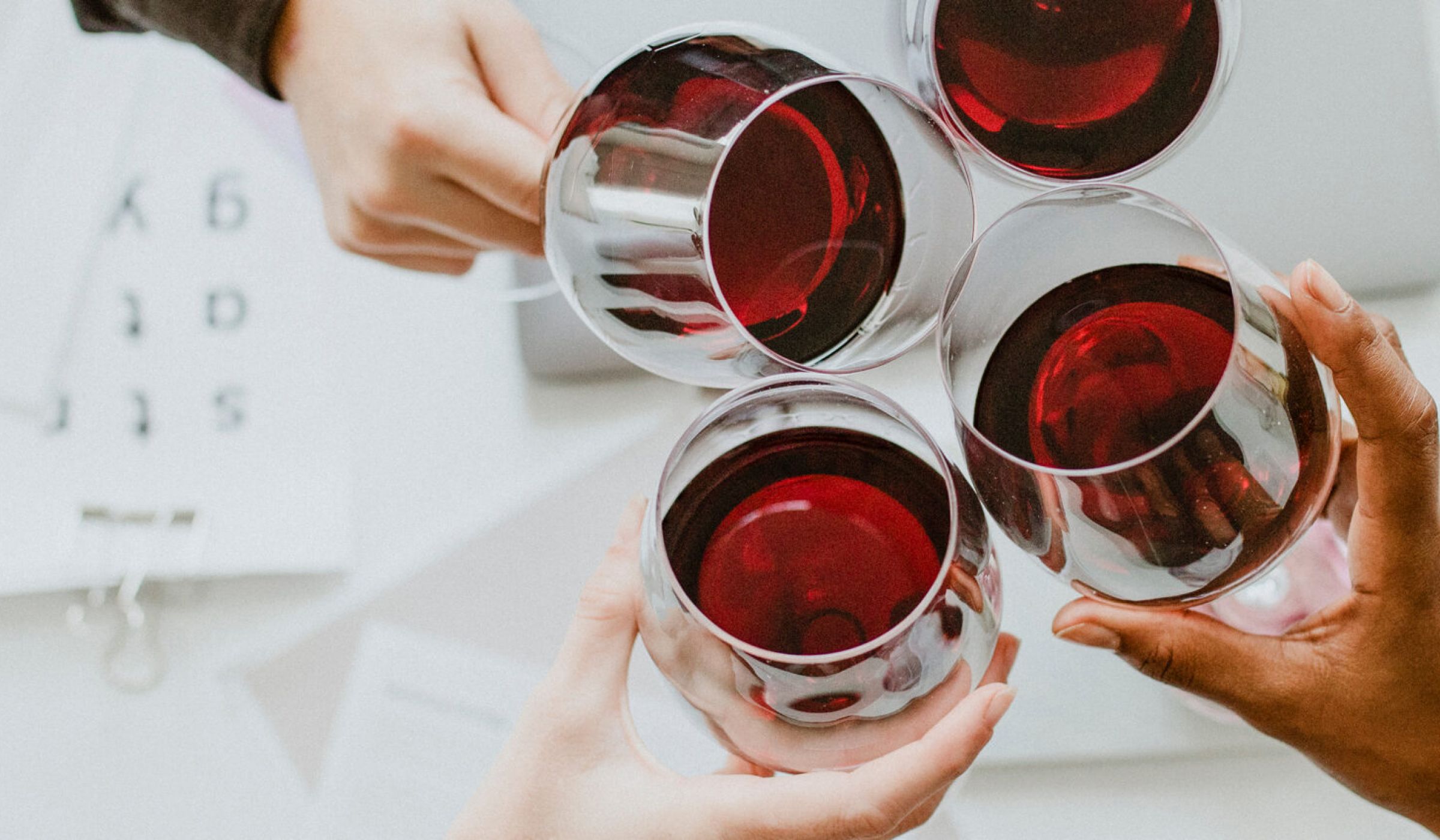 The Ensley 55+ Luxury Apartments with Four people toasting with glasses of red wine over a white table with papers and a small plant.