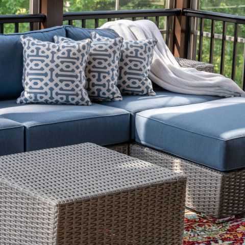 The Ensley 55+ Luxury Apartments with Blue outdoor sectional with patterned pillows, a knit blanket, and a wicker table on a colorful rug.