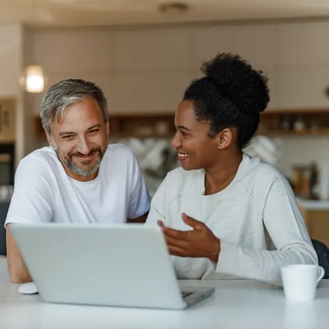 The Ensley 55+ Luxury Apartments with Two people sitting at a table, smiling and talking while looking at a laptop in a bright kitchen.