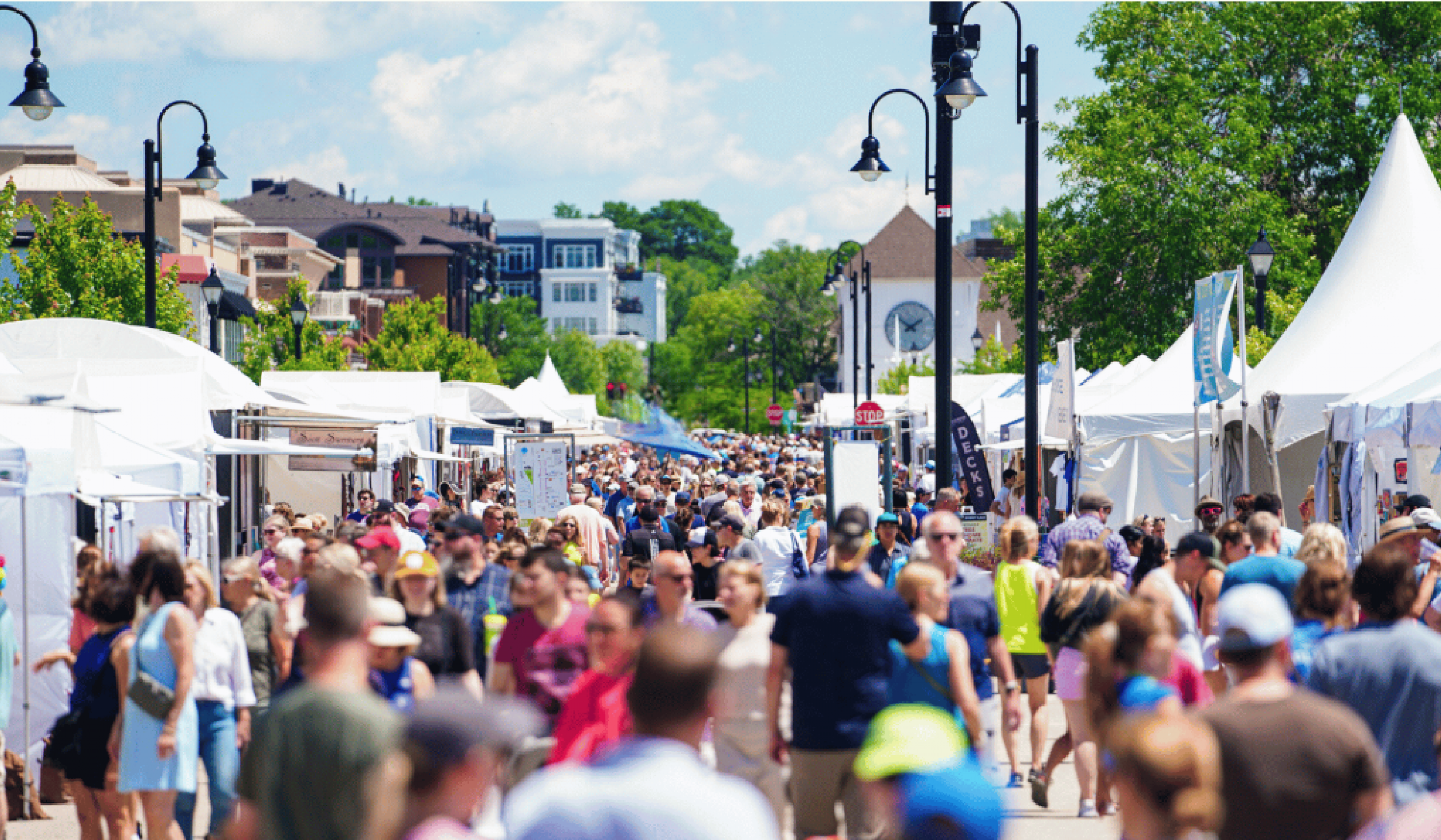 The Ensley 55+ Luxury Apartments with Crowd of people walking among white vendor tents at an outdoor street fair on a sunny day.