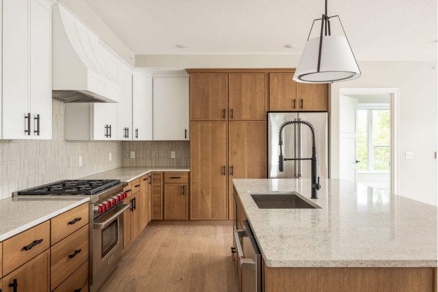 The Ensley 55+ Luxury Apartments with Modern kitchen with wood cabinets, white countertops, stainless appliances, large island, and a black gooseneck faucet.