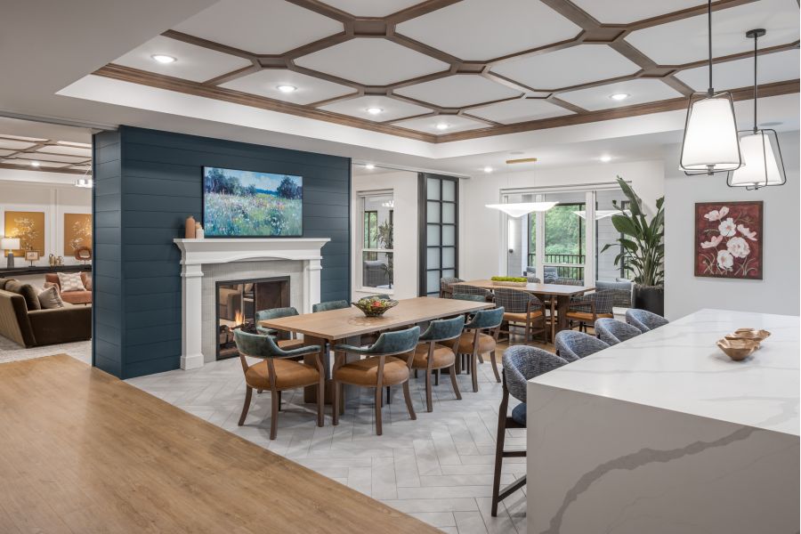 The Ensley 55+ Luxury Apartments with Modern open dining area with a wooden table, fireplace, art, and a view of the kitchen and living room.